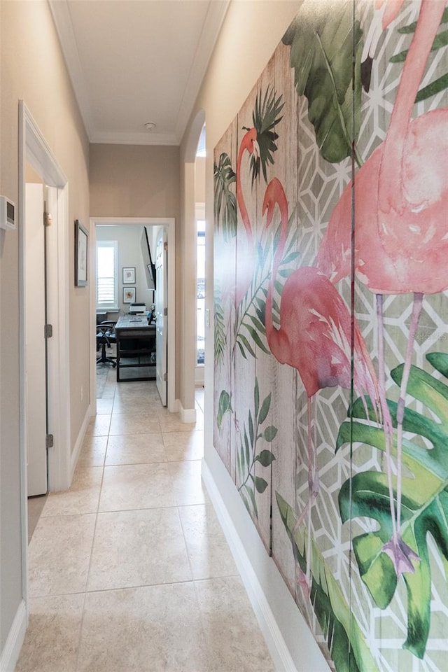 hallway with tile patterned floors, ornamental molding, baseboards, and arched walkways