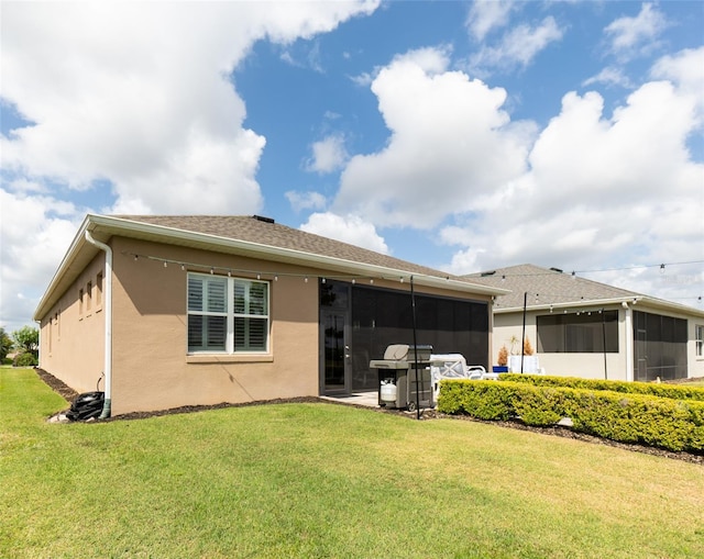 back of house with a sunroom, stucco siding, and a lawn