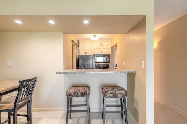 kitchen featuring a kitchen breakfast bar, white cabinetry, baseboards, black appliances, and recessed lighting