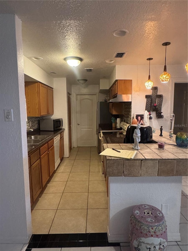 kitchen with brown cabinetry, a peninsula, visible vents, and stainless steel microwave