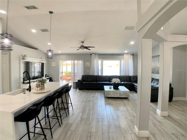 living room with light wood-style floors, visible vents, a ceiling fan, and arched walkways