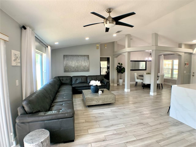 living area with lofted ceiling, decorative columns, light wood-style flooring, arched walkways, and a ceiling fan