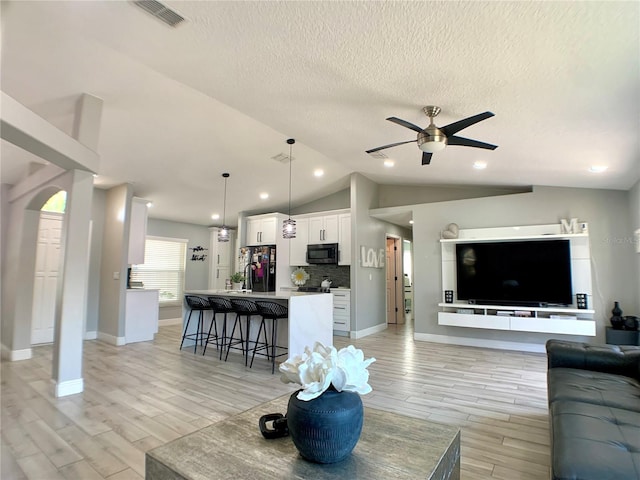 living area featuring a ceiling fan, light wood-style floors, visible vents, and vaulted ceiling