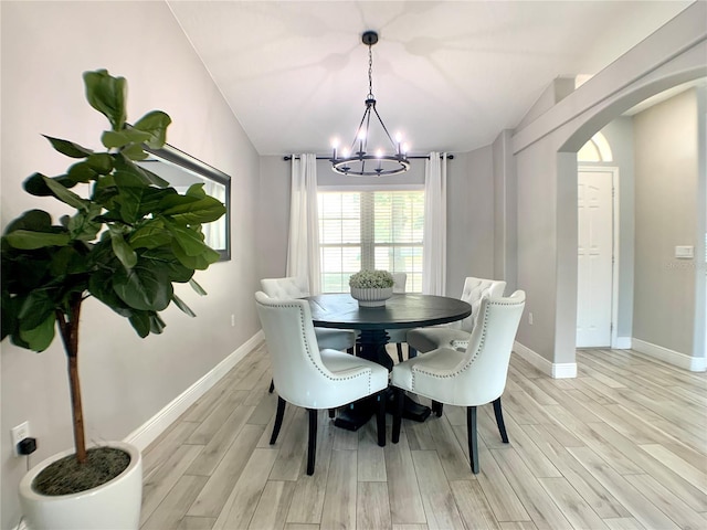 dining area with light wood-style flooring, baseboards, arched walkways, and a notable chandelier