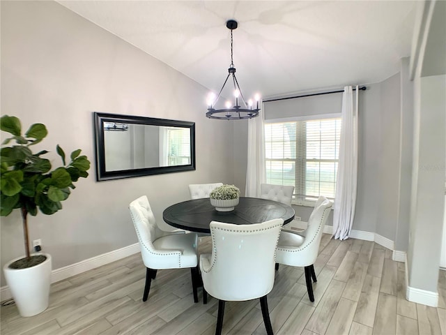 dining room with light wood-type flooring, baseboards, lofted ceiling, and a notable chandelier