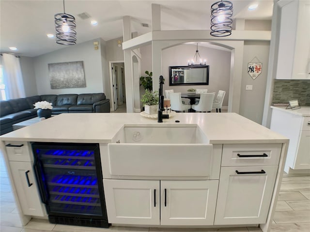 kitchen with a sink, vaulted ceiling, open floor plan, beverage cooler, and white cabinets