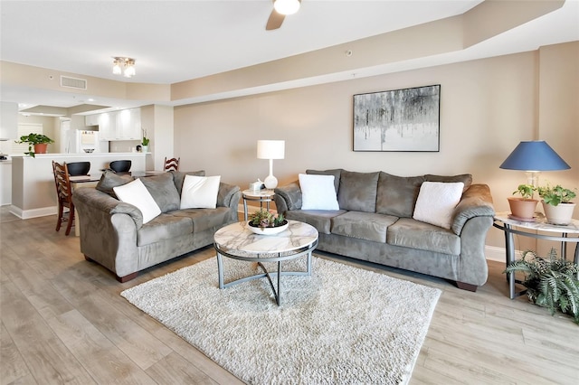 living area featuring light wood finished floors, baseboards, a ceiling fan, and visible vents