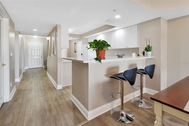 kitchen featuring light wood-style flooring, baseboards, a breakfast bar, visible vents, and white cabinets
