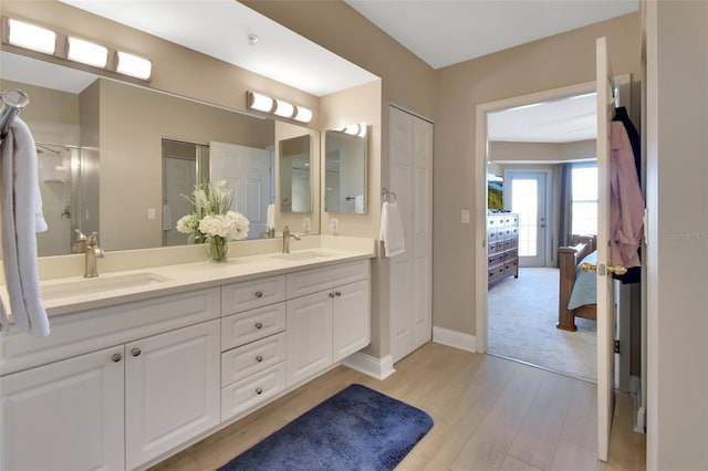 ensuite bathroom featuring a sink, double vanity, connected bathroom, and wood finished floors