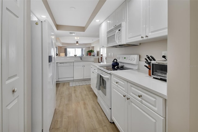 kitchen with a sink, white appliances, light wood finished floors, white cabinetry, and a ceiling fan