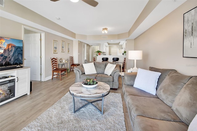 living room with light wood-type flooring, visible vents, baseboards, and a ceiling fan