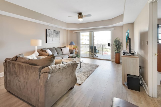 living area with a tray ceiling, ceiling fan, baseboards, and light wood-type flooring