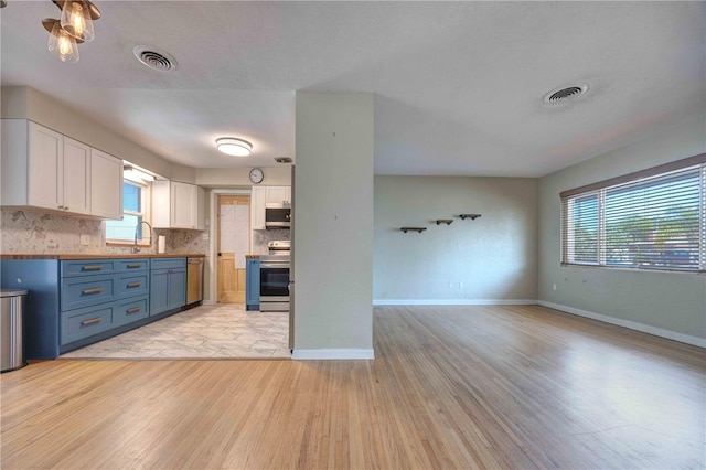 kitchen with appliances with stainless steel finishes, light wood finished floors, white cabinetry, tasteful backsplash, and baseboards