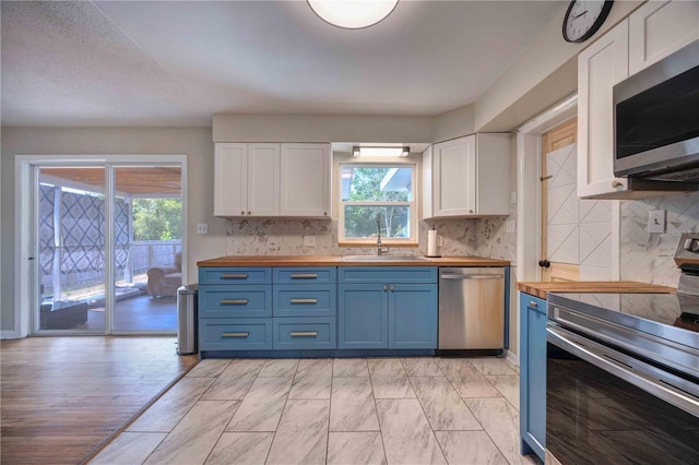 kitchen featuring stainless steel appliances, wooden counters, a sink, blue cabinets, and white cabinetry