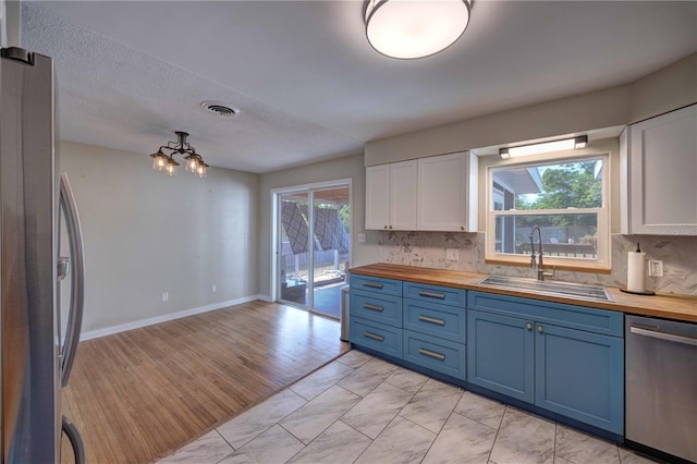 kitchen with butcher block counters, appliances with stainless steel finishes, a sink, and blue cabinetry