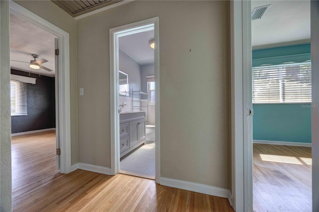 hall with light wood-type flooring, baseboards, and a sink