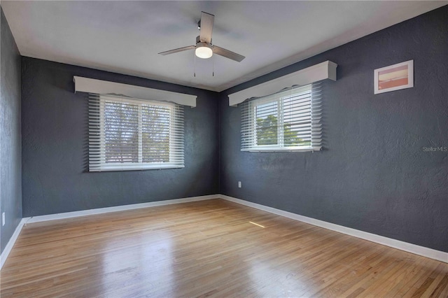 empty room with ceiling fan, wood finished floors, baseboards, and a textured wall