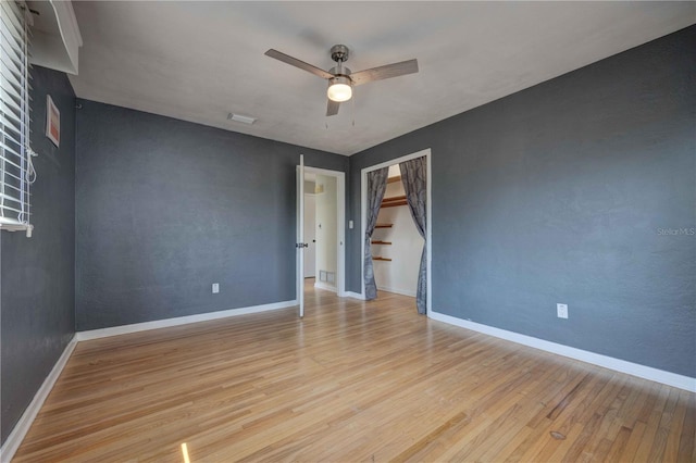 empty room with wood finished floors, a ceiling fan, baseboards, and stairway