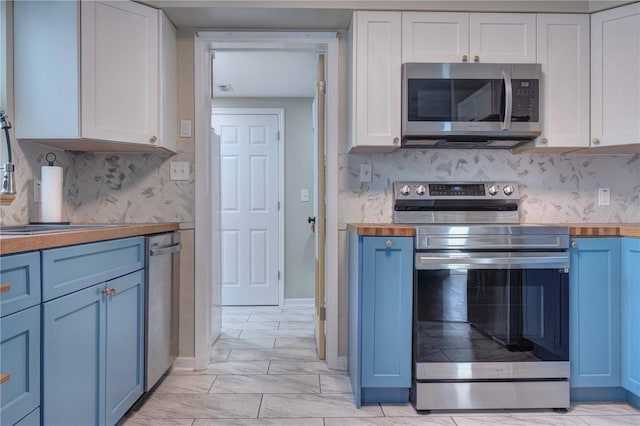 kitchen with stainless steel appliances, butcher block counters, white cabinetry, blue cabinetry, and backsplash