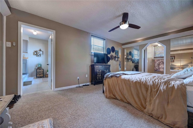 bedroom with light colored carpet, a textured ceiling, baseboards, and ceiling fan