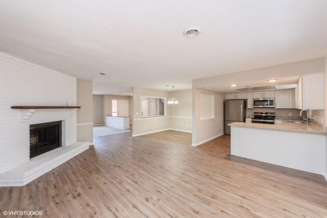 unfurnished living room featuring light wood finished floors, a fireplace, visible vents, and a sink