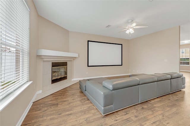 home theater with a ceiling fan, wood finished floors, a fireplace, and baseboards