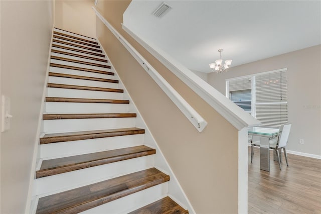 stairs with a chandelier, wood finished floors, and baseboards