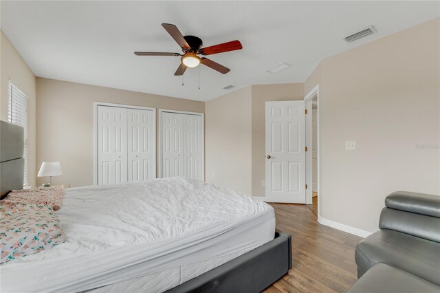 bedroom with two closets, wood finished floors, baseboards, and ceiling fan