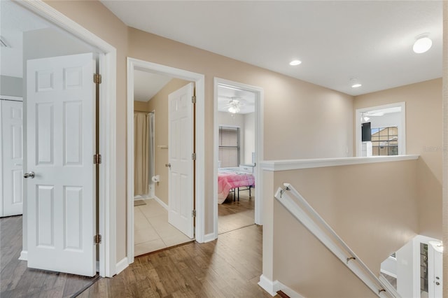 corridor featuring an upstairs landing, wood finished floors, baseboards, and recessed lighting