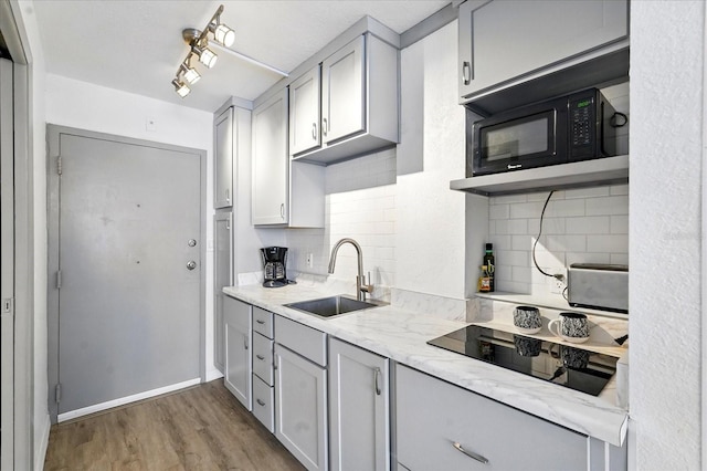 kitchen featuring black appliances, a sink, backsplash, wood finished floors, and gray cabinets