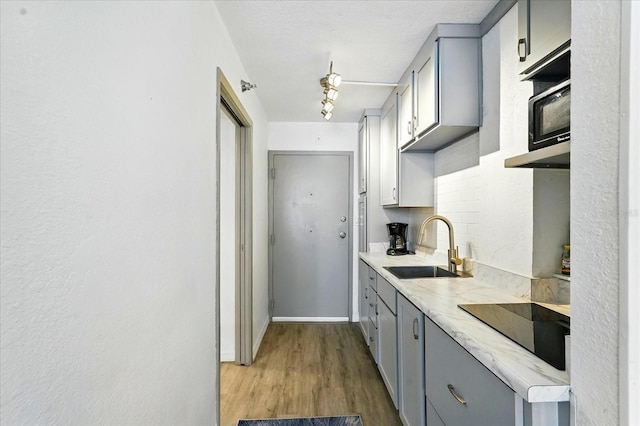 kitchen featuring gray cabinets, a sink, black electric stovetop, wood finished floors, and light countertops