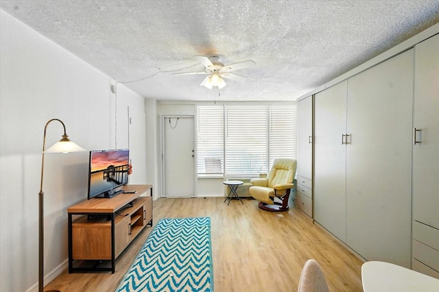 living area with light wood-type flooring, a ceiling fan, a textured ceiling, and baseboards