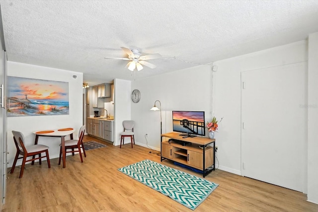 living area featuring light wood-style flooring, a textured ceiling, ceiling fan, and baseboards