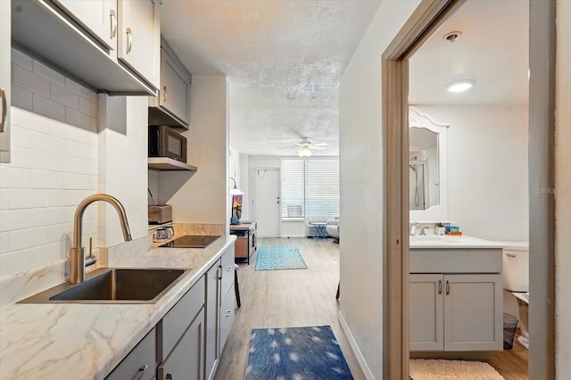 kitchen with a sink, gray cabinets, ceiling fan, light wood-style flooring, and a textured ceiling
