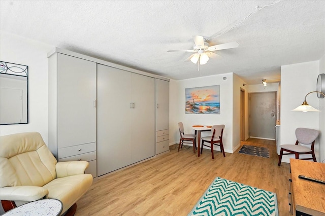 living area featuring a ceiling fan, light wood-type flooring, a textured ceiling, and baseboards
