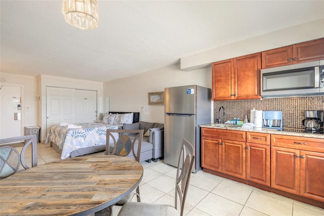 kitchen with appliances with stainless steel finishes, a sink, light tile patterned flooring, backsplash, and light stone countertops