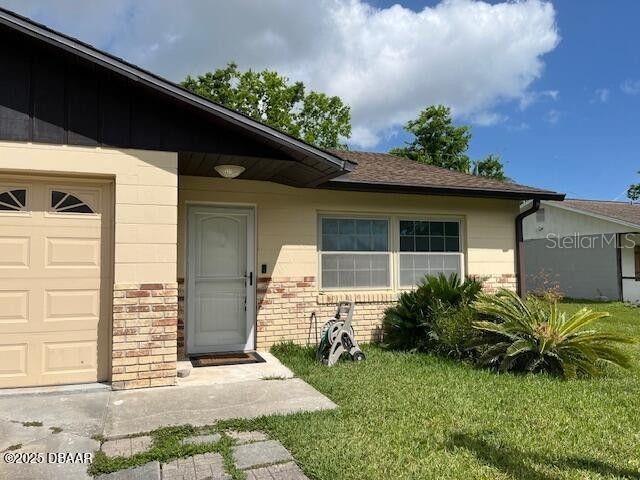 908 Boulder Dr, South Daytona, FL 32119 - view of exterior entry featuring a yard, brick siding, and an attached garage