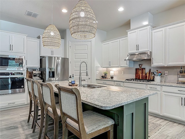 409 Nowell Loop, Deland, FL 32724 - kitchen featuring appliances with stainless steel finishes, a sink, under cabinet range hood, a center island with sink, and light stone countertops