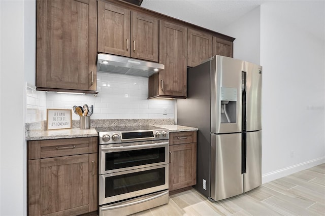 3322 Modena Way, New Smyrna Beach, FL 32168 - kitchen featuring appliances with stainless steel finishes, under cabinet range hood, backsplash, and light stone countertops