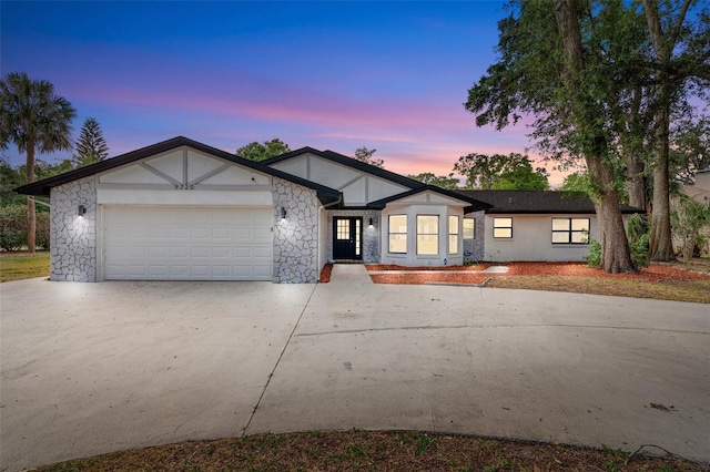 view of front of house featuring driveway, a garage, stone siding, and stucco siding