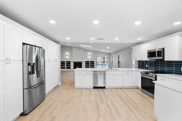 kitchen with appliances with stainless steel finishes, a peninsula, light wood finished floors, recessed lighting, and white cabinets