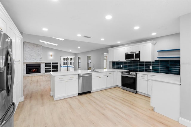 kitchen featuring appliances with stainless steel finishes, a peninsula, lofted ceiling, open floor plan, and a sink