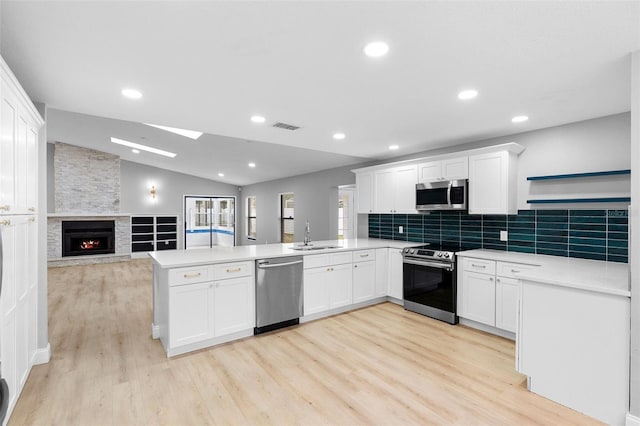 kitchen featuring stainless steel appliances, a peninsula, light wood-style flooring, vaulted ceiling, and white cabinetry