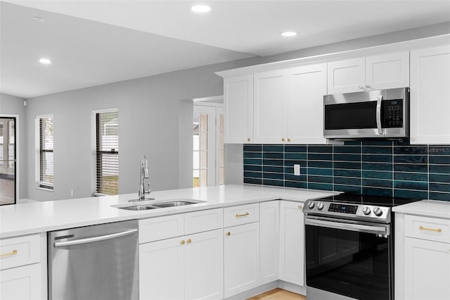 kitchen featuring appliances with stainless steel finishes, a sink, a peninsula, tasteful backsplash, and light countertops