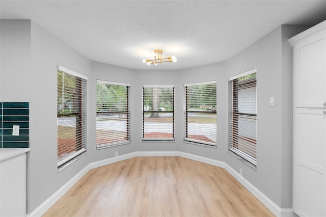 unfurnished dining area featuring light wood-style flooring, a chandelier, and baseboards