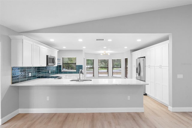 kitchen featuring stainless steel appliances, a peninsula, a sink, light wood-style flooring, and light countertops