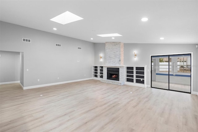 unfurnished living room with a skylight, recessed lighting, baseboards, light wood-style flooring, and a stone fireplace