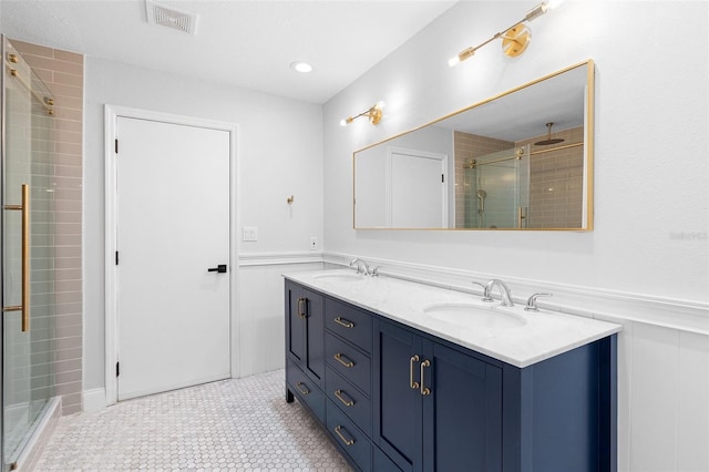 bathroom featuring a stall shower, wainscoting, double vanity, a decorative wall, and tile patterned floors