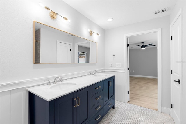 bathroom featuring a wainscoted wall, a ceiling fan, double vanity, and a decorative wall