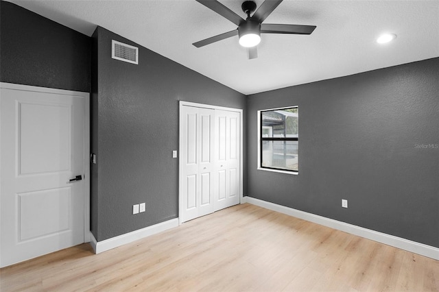 unfurnished bedroom featuring light wood finished floors, vaulted ceiling, a textured wall, a closet, and baseboards
